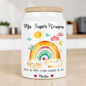 Peut inclure: Un bocal de rangement en céramique blanche avec un couvercle en bois, orné d'un arc-en-ciel, d'un soleil, d'une lune et de nuages à l'aquarelle. Il porte les inscriptions "Ma Super Nounou", "Merci de t'être si bien occupée de moi" et "Martin".