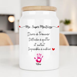 Peut inclure: Un pot en céramique blanc avec un couvercle en bois. Le pot porte l'inscription "Ma Super Maîtresse" et d'autres textes en français, ainsi qu'une empreinte de main rose et un cœur. Il s'agit probablement d'un cadeau ou d'un objet décoratif.
