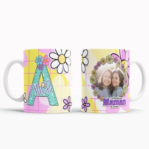 Peut inclure: Mug en céramique blanche avec un fond rose et jaune. Le mug présente une grande lettre "A" avec le nom "Alice" écrit en violet. Le mug a également un motif de marguerite et d'autres fleurs. L'autre côté du mug a une photo de deux femmes avec une couronne de fleurs autour de la photo. Le texte "La Meilleure Maman du monde" est écrit en violet.