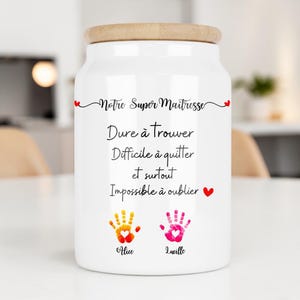 Peut inclure: Pot en céramique blanc avec un couvercle en bois. Le pot porte l'inscription "Notre Super Maîtresse" et d'autres textes en français, ainsi que deux empreintes de mains et les noms "Alice" et "Lucille".