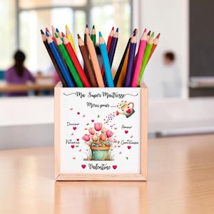 Peut inclure: Un pot à crayons en bois rempli de crayons de couleur. Le pot présente un motif floral avec le texte "Ma Super Maîtresse Merci pour..." et d'autres mots français. Un cadeau pour un professeur.