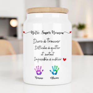 Peut inclure: Un pot en céramique blanc avec un couvercle en bois. Le pot porte l'inscription "Notre Super Nounou" et d'autres textes en français, ainsi que deux empreintes de mains et des noms. Un objet de décoration.