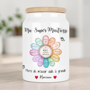 Peut inclure: Un pot en céramique blanc avec un couvercle en bois clair orné d'un motif floral aux pétales colorés portant des mots français, le texte "Ma Super Maitresse", "Merci de m'avoir aidé à grandir" et "Marceau" avec deux cœurs rouges.