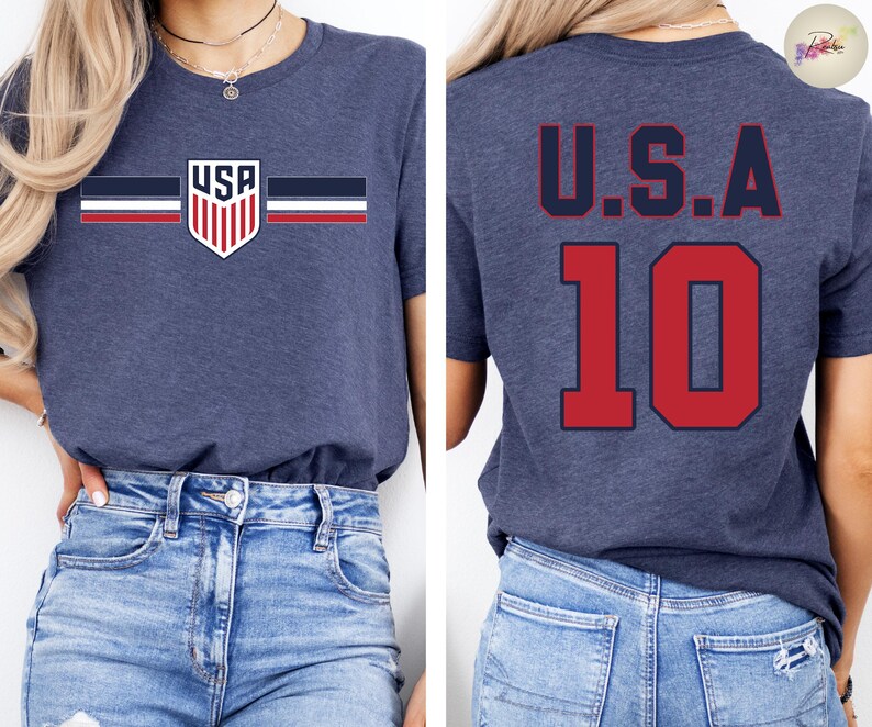 May include: A heather navy blue short-sleeve t-shirt. The front features a small shield graphic with the text USA and horizontal stripes in navy, white, and red. The back displays the text U.S.A. in navy above the large red number 10.