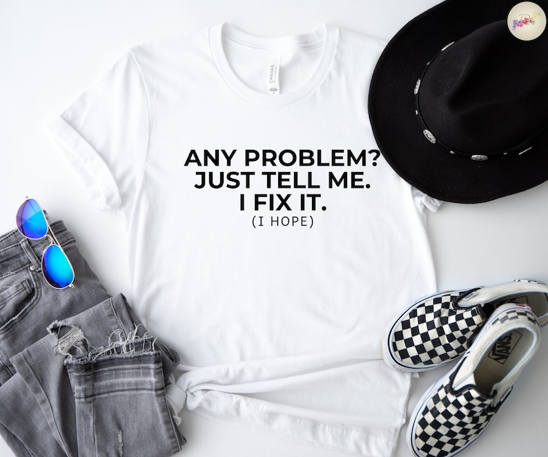 May include: A white t-shirt with the text "ANY PROBLEM? JUST TELL ME. I FIX IT. (I HOPE)". The shirt is paired with grey jeans, blue sunglasses, a black hat, and checkered slip-on shoes.