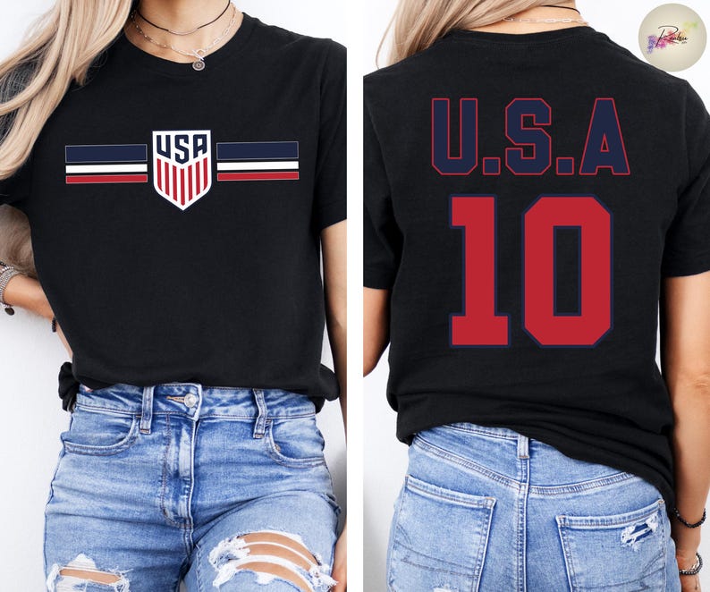 May include: A black short-sleeve t-shirt featuring a front graphic of a shield with the text USA and horizontal stripes in navy, white, and red. The back of the shirt displays the text U.S.A. in navy blue above the large red number 10.