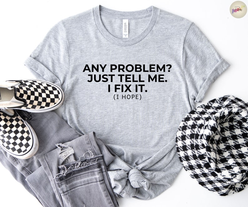 May include: A grey t-shirt with the text "ANY PROBLEM? JUST TELL ME. I FIX IT. (I HOPE)". The shirt is styled with grey jeans, black and white checkered slip-on shoes, and a black and white patterned hat.