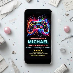 May include: A black and neon-colored digital invitation for a video game themed party. The invitation features a neon-colored video game controller with the text "Game On!" and the name "Michael" in a bright blue font. The text reads "Join us to celebrate Michael has reached level 10. Saturday, August 20, 2:00-5:00 PM at Michael's House, Edgewood Dr. Rochester, NY 14609. RSVP to Mia at 123.456.789."