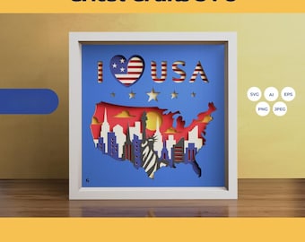 May include: A white frame with a blue background and a paper cut-out design of the United States with the words "I LOVE USA" and a heart with the American flag design.
