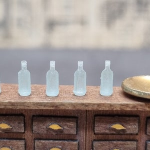 Könnte beinhalten: Sechs klare Glasflaschen mit mattem Finish stehen auf einem Holzregal mit Schubladen in einer Reihe. Die Flaschen sind alle gleich groß und haben die gleiche Form.