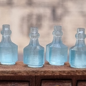 May include: Four clear glass bottles with a textured surface. The bottles are arranged in a row on a wooden surface.