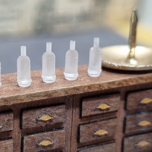 May include: A miniature wooden dresser with six drawers and gold-coloured drawer pulls. Five clear plastic bottles are arranged on the top of the dresser.