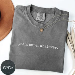 May include: A gray t-shirt with the text "yeah. sure. whatever." printed in white on the front.