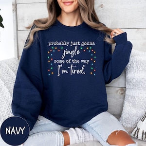 May include: Navy blue sweatshirt with the text "probably just gonna jingle some of the way I'm tired." The text is surrounded by a string of colorful Christmas lights. The word "NAVY" is in a navy circle in the bottom left corner.