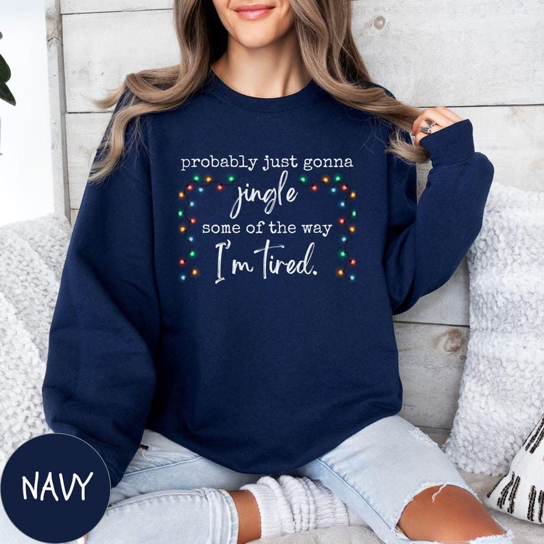 May include: Navy blue sweatshirt with the text "probably just gonna jingle some of the way I'm tired." The text is surrounded by a string of colorful Christmas lights. The word "NAVY" is in a navy circle in the bottom left corner.