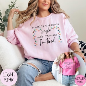 May include: Light pink sweatshirt with the text "probably just gonna jingle some of the way I'm tired" framed by a string of colorful lights. The image also shows a smaller image of a pink t-shirt with the same text.
