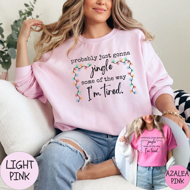 May include: Light pink sweatshirt with the text "probably just gonna jingle some of the way I'm tired" framed by a string of colorful lights. The image also shows a smaller image of a pink t-shirt with the same text.