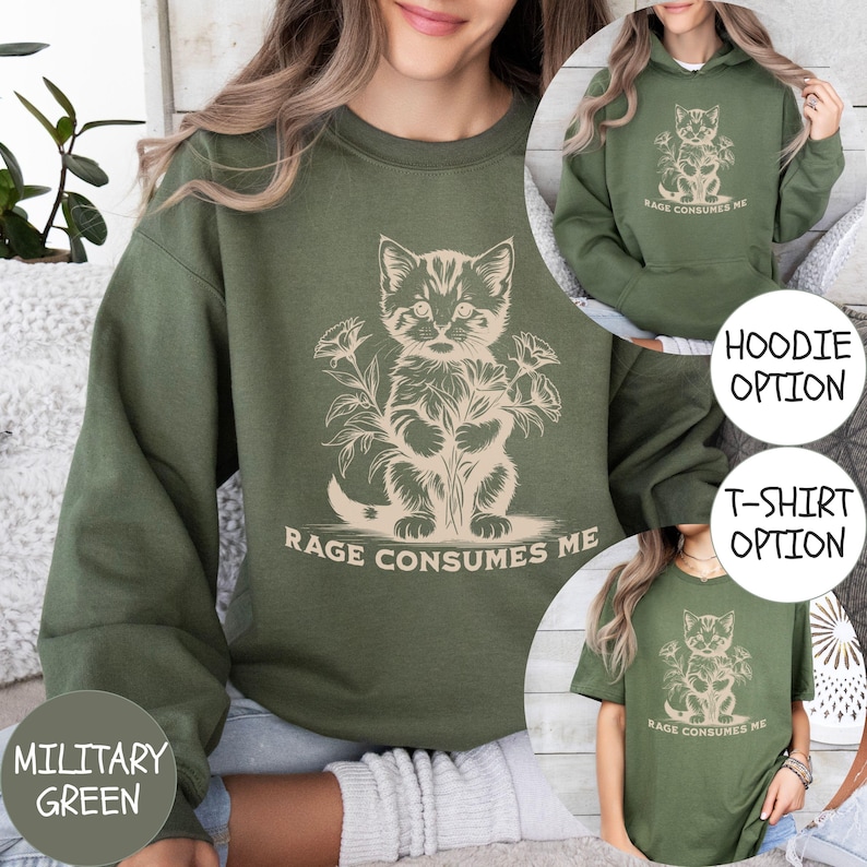 Puede incluir: Una sudadera verde con un gr&aacute;fico de un gato sosteniendo flores y el texto "Rage Consumes Me". La sudadera est&aacute; disponible en opci&oacute;n de sudadera con capucha y camiseta.