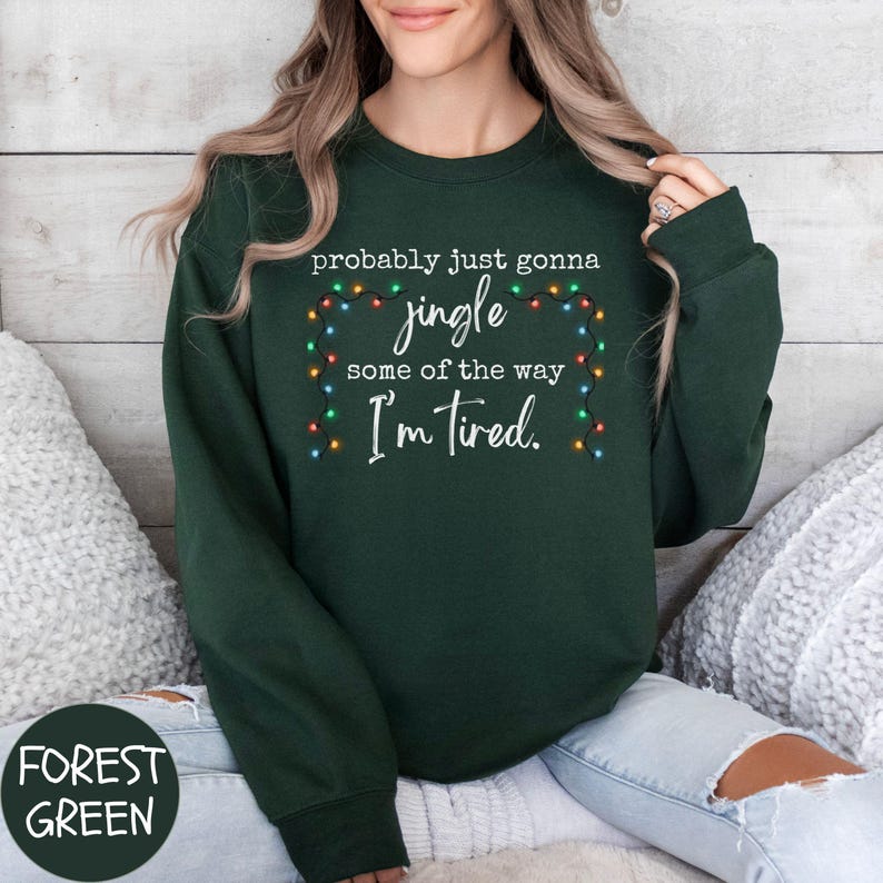 May include: Forest green sweatshirt with the text "probably just gonna jingle some of the way I'm tired." The text is in white with a string of colorful Christmas lights. The sweatshirt is a solid color.