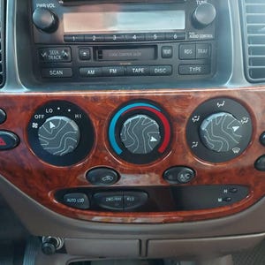 Könnte beinhalten: Nahaufnahme eines Armaturenbretts mit Holzmaserung. Es zeigt ein Radio mit Tasten für AM/FM, Kassette und CD. Schwarze Klimaregler mit weißen Markierungen. Es gibt auch verschiedene Knöpfe.