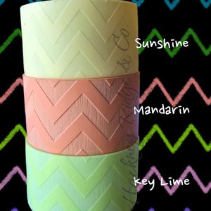 May include: Three stacked, cylindrical containers in pastel colors: sunshine yellow, mandarin orange, and key lime green. Each container features a chevron pattern. The background is black with colorful zigzag lines.