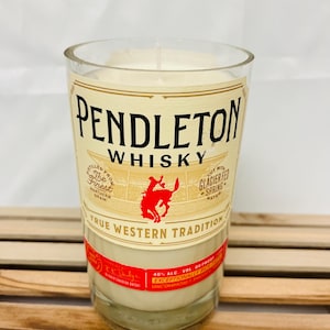 May include: A clear glass candle jar with a white candle inside. The jar is labeled with a vintage-style design that says "Pendleton Whisky" and features a cowboy riding a horse. The label also includes the text "True Western Tradition".
