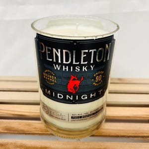 May include: A clear glass candle jar with a white candle inside. The jar is labeled with a black and white image of a horse and the text "PENDLETON WHISKY MIDNIGHT 90 PROOF".