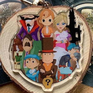 Könnte beinhalten: Ein Holzschlüsselanhänger mit einem transparenten Acryleinsatz, der eine Gruppe von Comicfiguren zeigt. Zu den Figuren gehören ein Mann mit einem Zylinder, eine Frau mit einem rosa Kleid, ein Mann mit einem violetten Anzug, eine Frau mit einem braunen Kleid, ein Mann mit einem blauen Hut und ein Hund. Der Schlüsselanhänger zeigt auch ein Fragezeichen in einem Apfel.