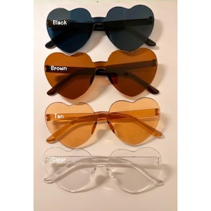 May include: Four pairs of heart-shaped sunglasses in black, brown, tan, and clear. The sunglasses have a rimless design and are arranged vertically. The colours are labelled on the image.