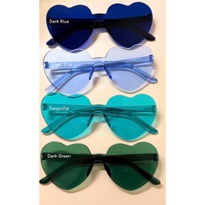 May include: Four pairs of heart-shaped sunglasses in various colors: dark blue, light blue, turquoise, and dark green. Each pair has a matching frame and lenses. The text labels each color.