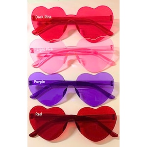 May include: Four pairs of heart-shaped sunglasses in shades of dark pink, light pink, purple, and red. Each pair has a rimless design with a heart-shaped lens and matching arms. The text "Dark Pink", "Light Pink", "Purple", and "Red" are visible.