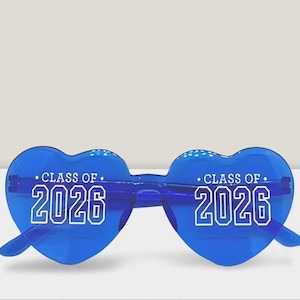 May include: Blue heart-shaped sunglasses with the text "CLASS OF 2026" in white. The sunglasses have a clear frame and lenses. A fun accessory for graduation celebrations.