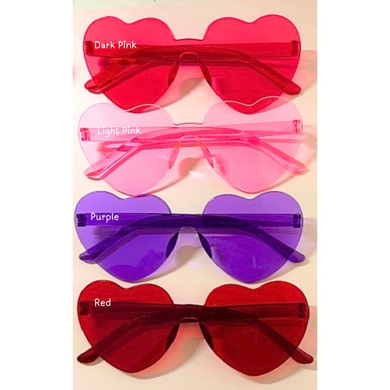 May include: Four pairs of heart-shaped sunglasses in shades of dark pink, light pink, purple, and red. Each pair has a rimless design with a heart-shaped lens and matching arms. The text "Dark Pink", "Light Pink", "Purple", and "Red" are visible.