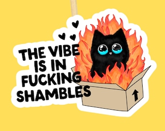 May include: A sticker depicting a black cat with large blue eyes, engulfed in flames, within a cardboard box. The text "THE VIBE IS IN FUCKING SHAMBLES" is printed in black. The background is a bright yellow.