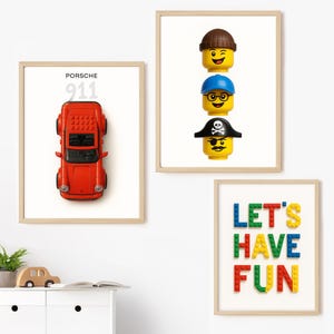 以下が含まれることがあります： 白い背景の3つの額入りプリント。1つは「PORSCHE 911」の文字が入った赤いおもちゃの車です。もう1つは3つのレゴの頭です。3つ目のプリントは、カラフルなレゴブロックで「LET'S HAVE FUN」と書かれています。