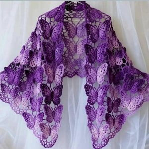 May include: A handcrafted crochet shawl in varying shades of purple, adorned with a butterfly pattern. The shawl is meticulously made with openwork and butterfly shapes, giving it a delicate and airy look. The colour gradient goes from dark purple to light lavender.