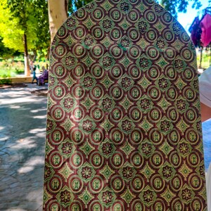 May include: A close-up of a fabric swatch with a repeating pattern of green, red, and gold circles and squares. The fabric has a textured surface.