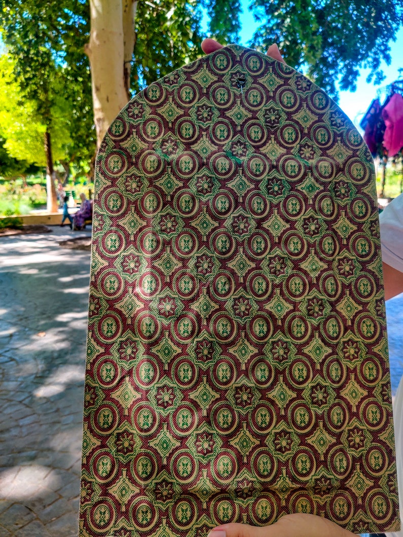May include: A close-up of a fabric swatch with a repeating pattern of green, red, and gold circles and squares. The fabric has a textured surface.
