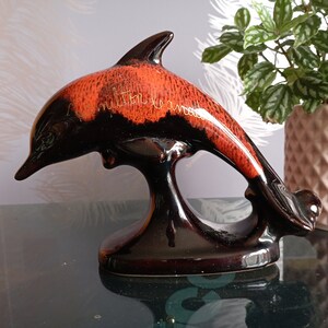 May include: A black and orange ceramic dolphin figurine with gold lettering that reads "Imitation is a mess".