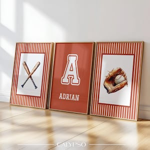 Peut inclure: Trois impressions encadrées sur le thème du baseball. L'une présente des battes croisées, une autre une grande lettre "A" avec le nom "ADRIAN", et la troisième un gant de baseball avec une balle. Les cadres ont une bordure dorée et un fond à rayures rouges et blanches.