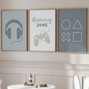 May include: Three framed prints with a gaming theme. The left print features a pair of headphones, the middle print says "gaming zone" with a video game controller, and the right print has four symbols from a video game controller.