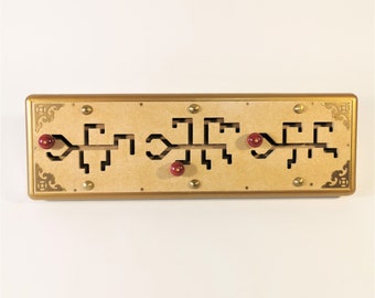 Puede incluir: Un rompecabezas rectangular de madera con marco dorado y detalles decorativos en las esquinas. El rompecabezas presenta formas recortadas y tres perillas rojas. Remaches de color latón aseguran las piezas de madera. El rompecabezas está diseñado para resolver problemas y entretener.