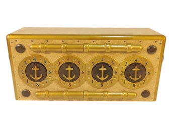 Puede incluir: Una caja de color dorado con cuatro diales redondos, cada uno con un ancla negra y los números del 1 al 8. La caja tiene una superficie texturizada y un borde dorado.