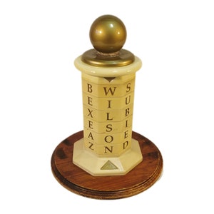May include: A vintage wooden letter game with a gold top and a white base. The letters spell out "WILSON" on the sides of the base.