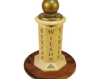 Puede incluir: Un juego de letras de madera vintage con una parte superior dorada y una base blanca. Las letras deletrean "WILSON" en los lados de la base.
