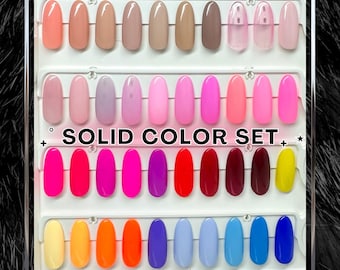 May include: A display board featuring rows of oval-shaped nail polish swatches in a wide variety of colors, including nudes, pinks, reds, yellows, and blues. The text SOLID COLOR SET is printed in black in the center of the white display board.