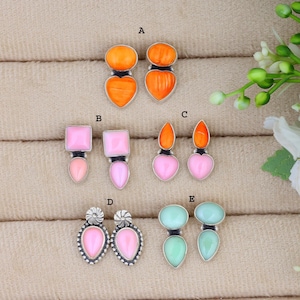 Könnte beinhalten: Fünf Ohrringpaare, beschriftet von A bis E. Paar A hat orangefarbene Steine, B hat quadratische rosa Steine, C hat orangefarbene und rosa Steine, D hat tropfenförmige rosa Steine mit Silberdetails und E hat hellgrüne Steine. Alle sind in Silber gefasst.