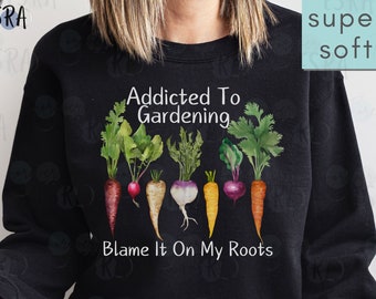 May include: Black sweatshirt with the text "Addicted To Gardening" and "Blame It On My Roots". The text is surrounded by a watercolor illustration of various vegetables, including carrots, radishes, and turnips. The sweatshirt is available in t-shirts too.