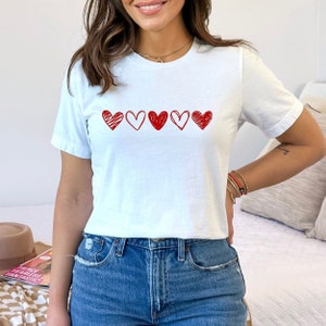 May include: White t-shirt with a row of five red hand-drawn hearts.
