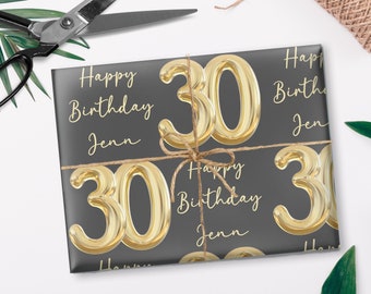 May include: Gray gift wrap with a repeating pattern of gold foil balloons shaped like the number 30. The text "Happy Birthday Jenn" is repeated on the wrap.